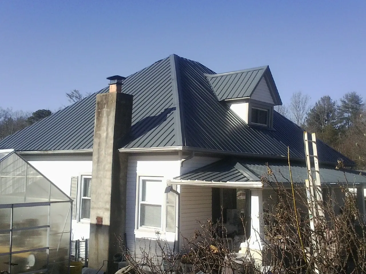 Dark blue standing seam metal roof on a white farmhouse with dormer — Slate & Tile Roof Repair by Roofing Brothers in Deming