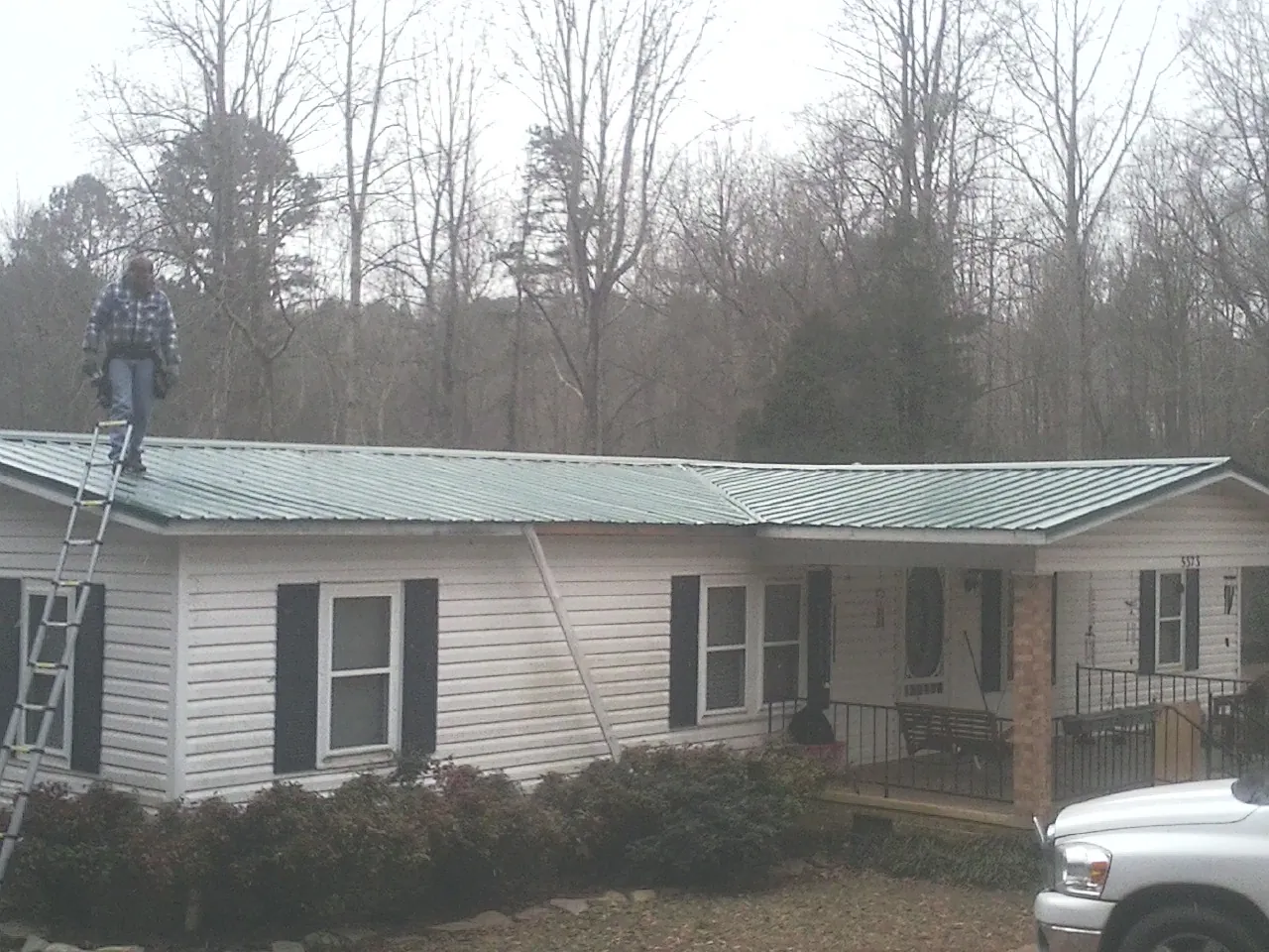 Worker on a ladder beside a new green metal roof on a ranch home in Deming