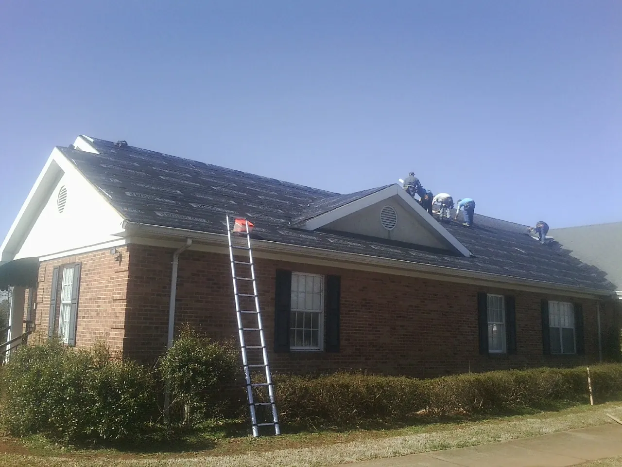 Crew tearing shingles off a brick ranch roof with a ladder set — Metal Roof Repair work by our crew in Deming