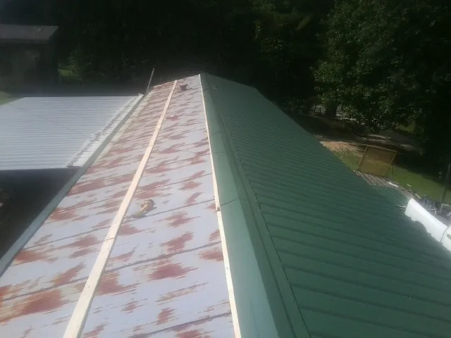 Old rusted panels beside newly installed green metal roofing — Wind Damage Roof Repair by Roofing Brothers in Deming